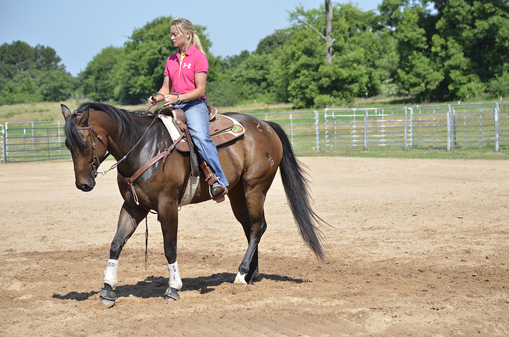 As she occasionally does when working around actual barrels, Janna will stop her horse and back him away from the barrel before asking him to step across with shoulder. Then she will pick up her hand to turn the barrel.