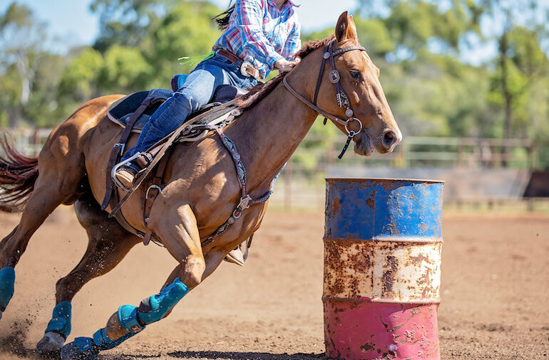 a barrel racer riding a performance horse around a barrel